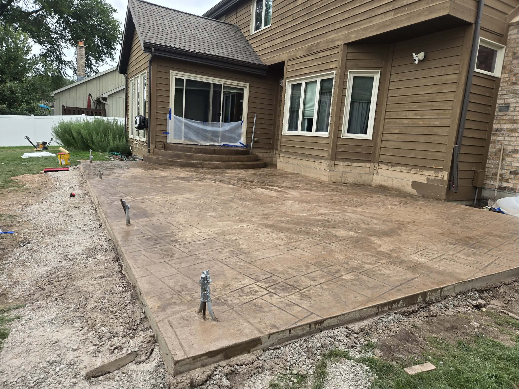 Large stamped concrete patio with steps behind a home, freshly poured